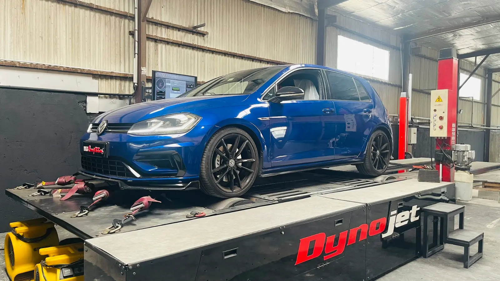 Une voiture sanglée sur les rouleaux du banc de puissance Dynojet, dans l'atelier.