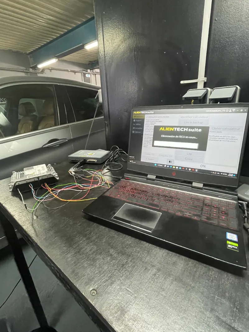 Un calculateur moteur posé sur l'établi, relié à l'outil de reprogrammation.